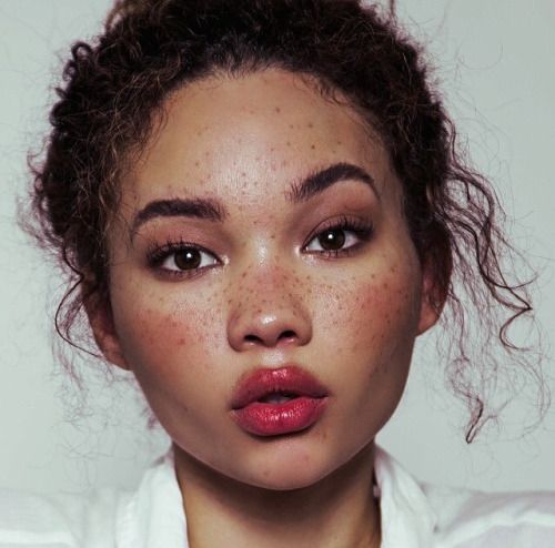 a closeup portrait of a woman with light skin, freckles, curly hair, and brown eyes. she is wearing lipstick, and her lips are slightly parted.