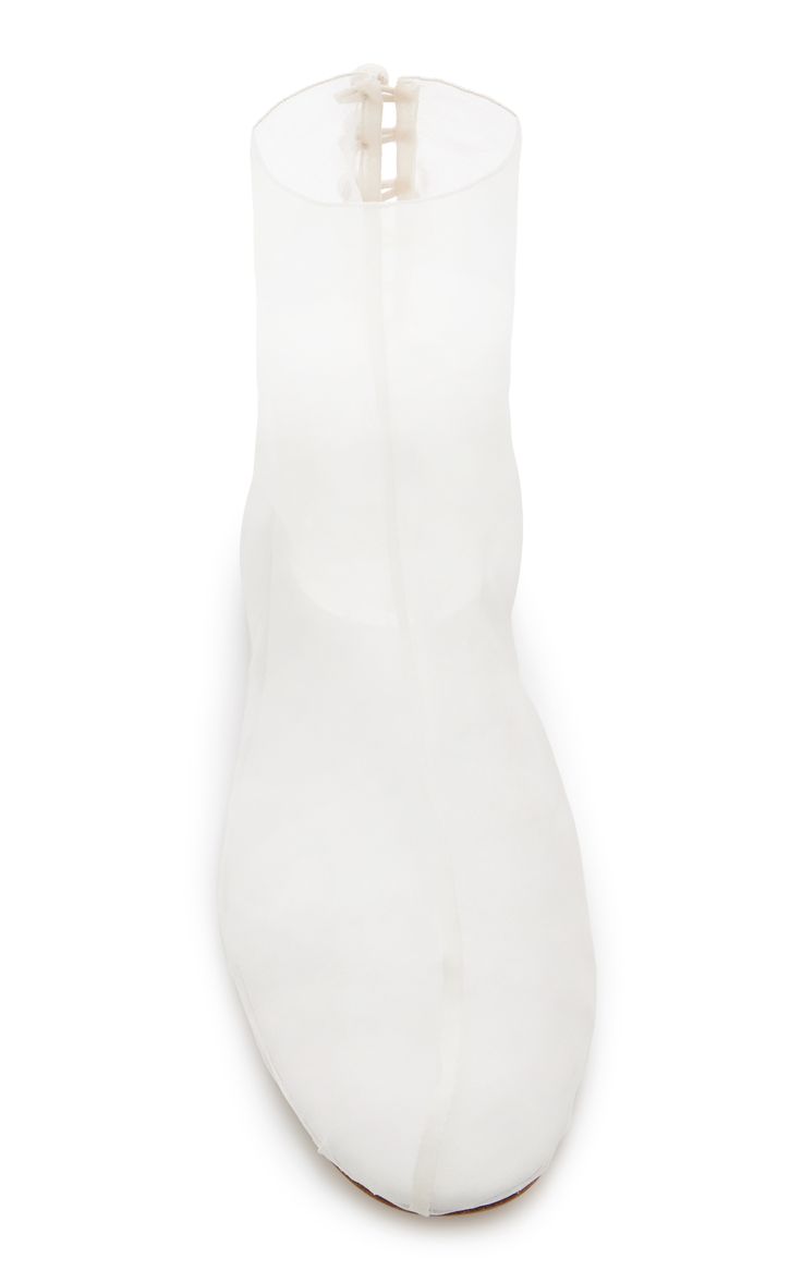 a topdown closeup shot showcases a pair of women's white, transparent ankle boots.  the boots are made from a seemingly sheer, possibly plastic or rubberlike material, giving them a minimalist and modern aesthetic.  the design is simple and elegant, with a smooth, rounded toe and a subtle back zipper detail. the boots are positioned against a clean white background, highlighting their translucent quality and sleek silhouette.