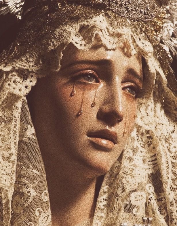 a closeup image of a statue depicting the virgin mary, her face adorned with tears rendered in gold. she wears an ornate crown and a delicate lace veil. the lighting is soft and warm, casting subtle shadows that emphasize the sorrowful expression on her face. the overall aesthetic evokes a sense of religious devotion and contemplation.