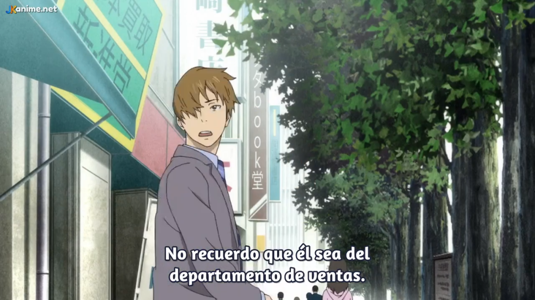 an anime screenshot of a young man with short brown hair wearing a gray suit and purple tie standing on a city sidewalk. he looks confused. the sky is overcast, creating natural, soft lighting. the image is taken from street level and shows buildings and leafy trees lining the sidewalk. there are japanese signs on the buildings.