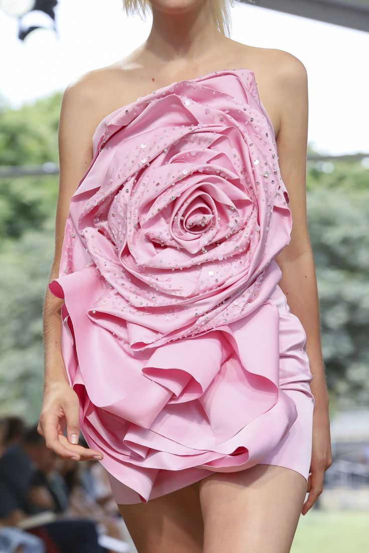 a model is wearing a pink, strapless dress with a large rose design on the front and sequins sprinkled throughout.