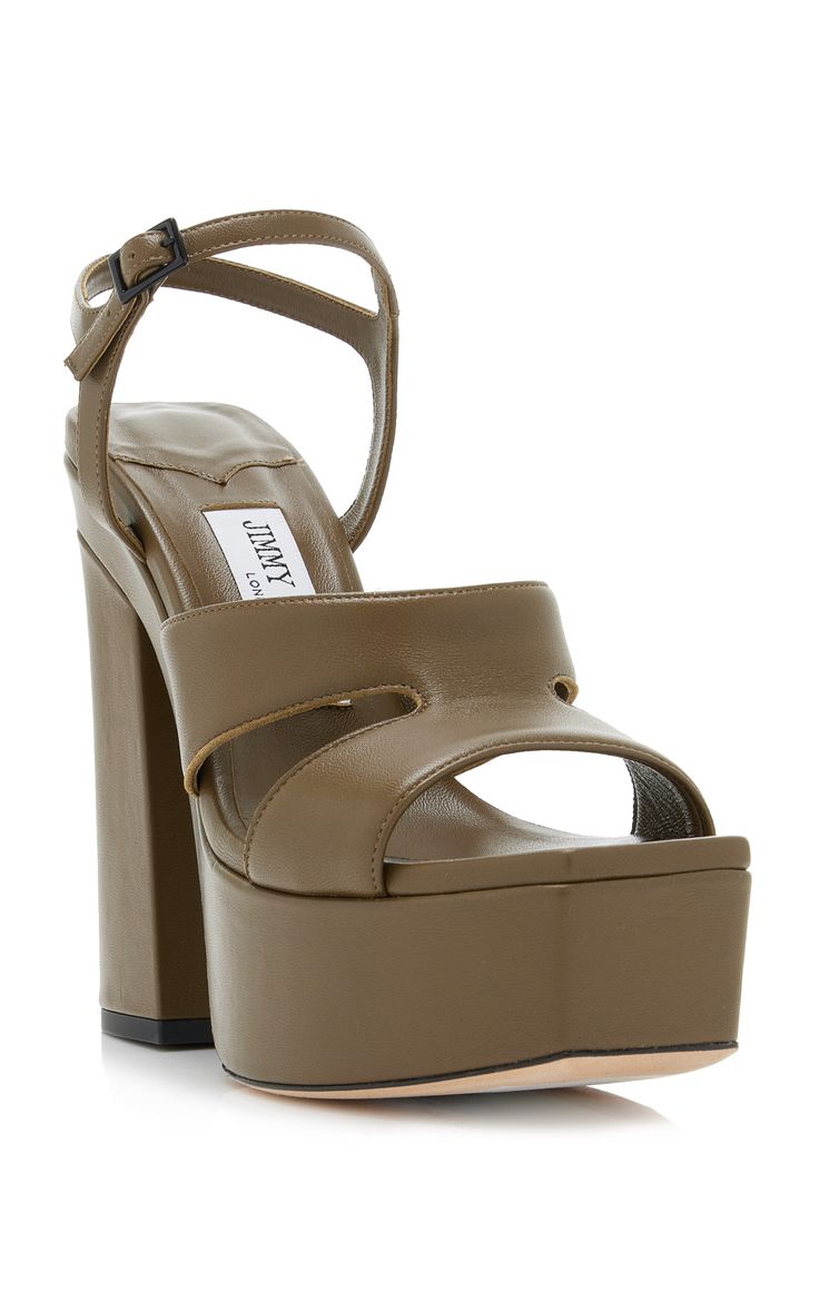 a pair of olive green leather jimmy choo platform sandals are displayed on a white background. the sandals feature a chunky heel, ankle strap, and cutout detail on the upper.  the jimmy choo label is visible inside the shoe. the sandals are positioned at a slight angle, showcasing their design and features.