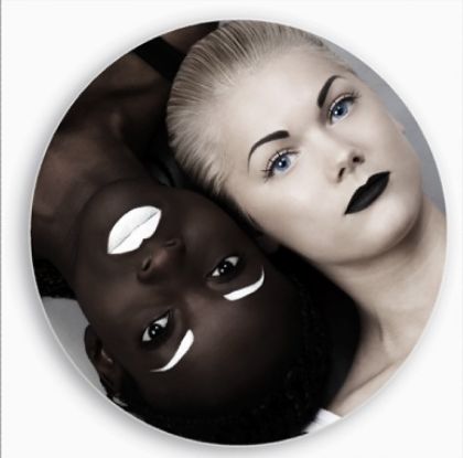 a close up portrait of two women with contrasting skin tones. the woman on the left has dark skin and white makeup, while the woman on the right has light skin and black makeup. the image is a strong visual representation of contrast and duality.