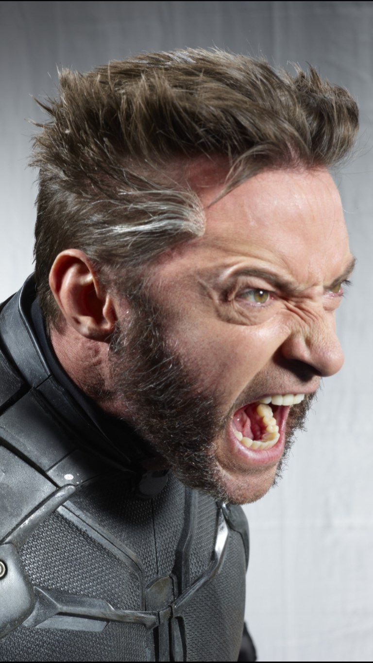 this is a profile portrait of hugh jackman as wolverine. he is snarling with an aggressive expression, revealing his teeth. he has a beard, styled hair with gray streaks, and is wearing a dark costume. the image suggests anger and intensity.