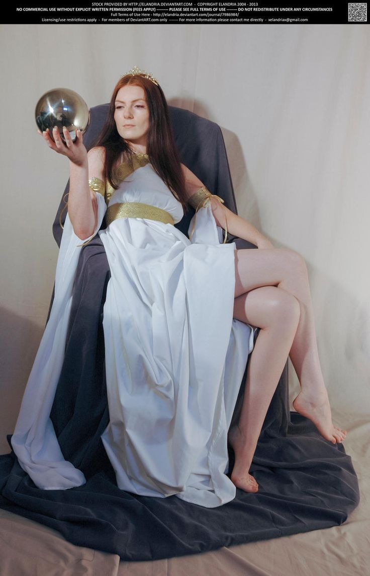 a woman in a white dress with gold accents sits in a chair and holds a silver orb.  she is posed with one leg crossed over the other and her left arm is extended towards the viewer. her gaze is direct, and her hair is styled with a crown.  the image has a fantasy and art nouveau feel.