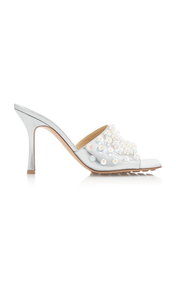 he image shows a pair of women's silver metallic leather mules with pearl embellishments. the shoes have a square toe and a high stiletto heel.  they are presented on a white background, showcasing the shoes' details and design.  the style appears to be elegant and suitable for formal occasions.