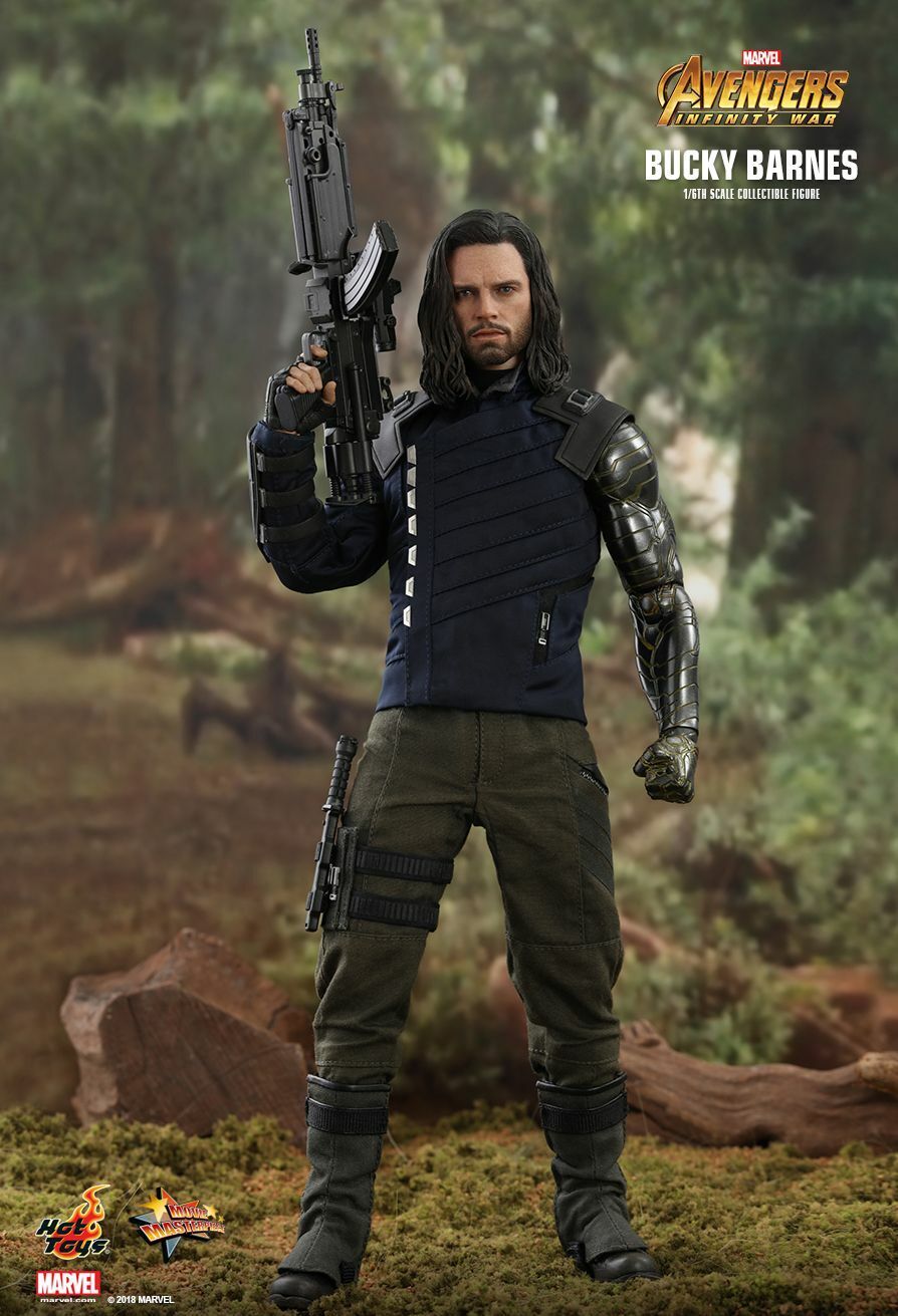 this is a promotional image of a 1/6 scale collectible figure of bucky barnes (the winter soldier) from avengers: infinity war, produced by hot toys. the figure is highly detailed, accurately replicating bucky's appearance in the film, including his dark blue tactical vest, olive green pants, black boots, and his signature metal arm.  he is holding a rifle and is posed in a forest setting.  the image includes the marvel and hot toys logos.