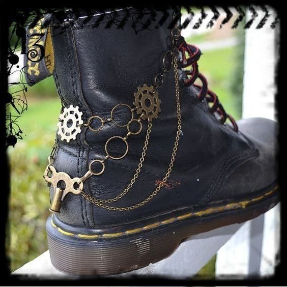 the image showcases a closeup view of a black leather boot adorned with a handcrafted steampunkstyle ankle bracelet. the bracelet features brass gears, chains, and a keyshaped charm, all intricately linked together.  the boot itself appears wellworn, adding to the overall aesthetic of the piece. the background is blurred but shows some greenery, suggesting an outdoor setting. the overall style is dark, grungy, and distinctly steampunk.