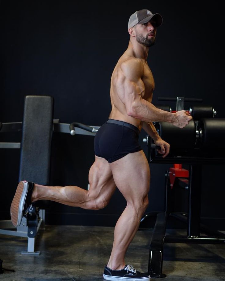 a muscular man in black athletic wear is working out at the gym. he is doing a leg exercise on a machine, using weights to build muscle. his legs are toned and muscular. he is focused on the exercise and is pushing himself to his limits.  he has a serious look on his face, showing his determination. he is a bodybuilder and is clearly committed to his fitness goals.