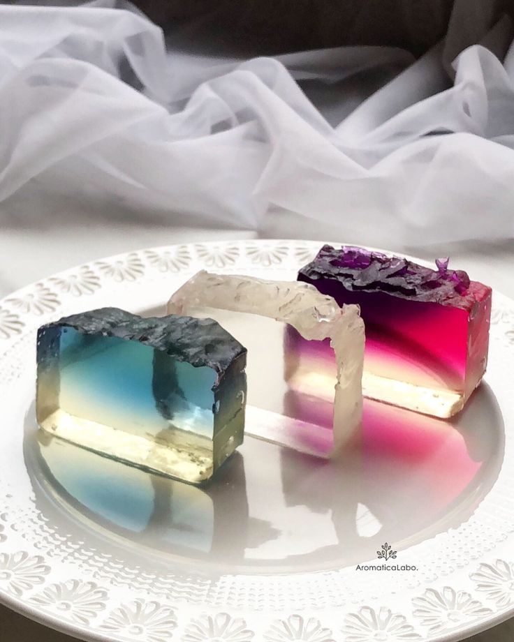 a closeup of three colorful clear jelly desserts on a white plate with an elegant design. the jelly is a gradient of colors from blue to pink and purple, creating a beautiful and visually appealing dessert.