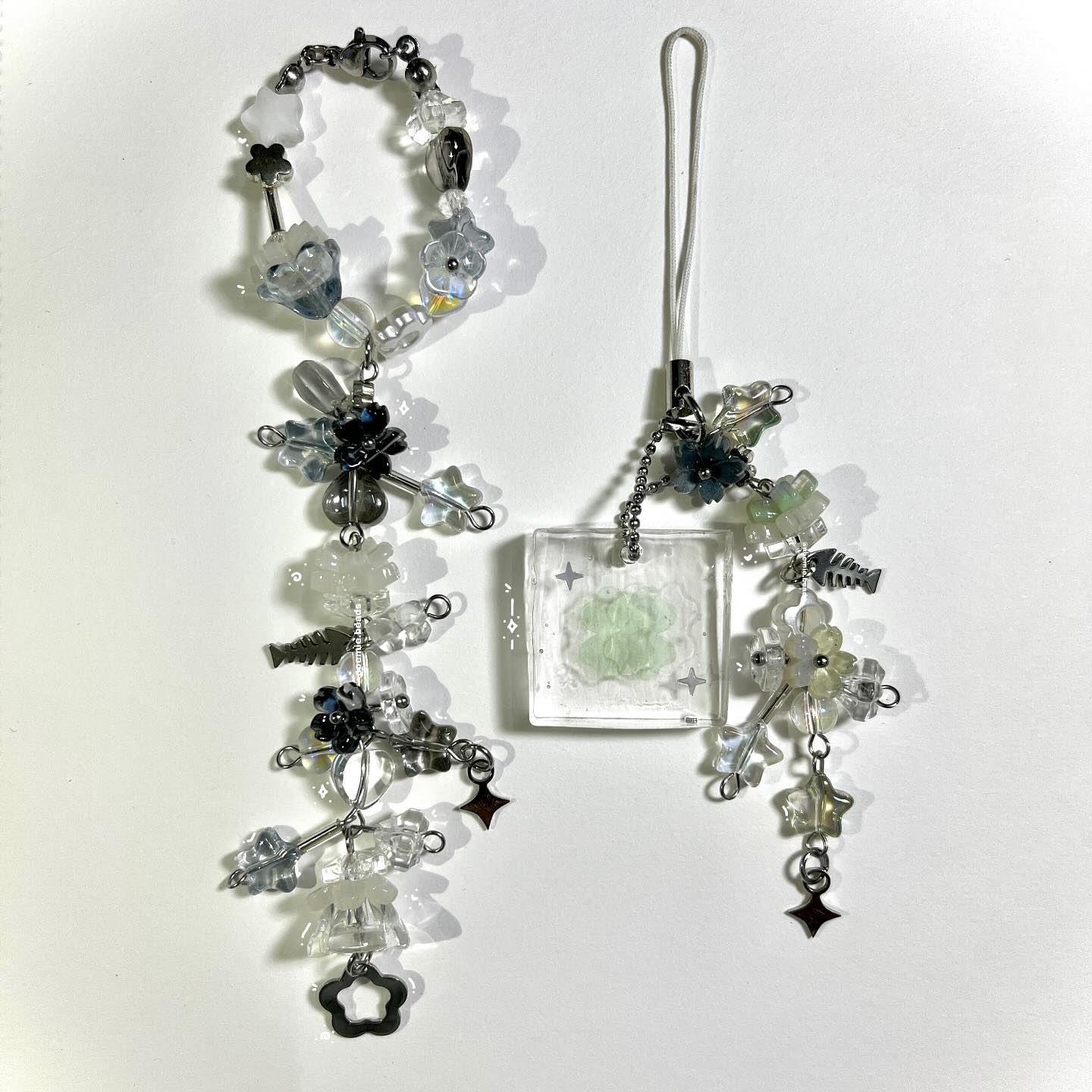 two pieces of handmade beaded jewelry are displayed on a white surface. the jewelry consists of beads, flowers, and pendants. one piece resembles a bracelet, while the other is a phone charm with a resin charm.