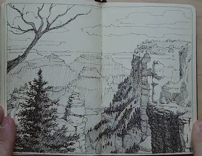 the image is a sketch of a canyon landscape drawn in a notebook. it depicts a vast canyon with rugged cliffs, mountains, and a cloudy sky. a bare tree and a conifer tree are in the foreground on the left side. the drawing is rendered with ink, creating detailed textures and shadows. the open notebook is held by hands, suggesting that this is a field sketch done on location.