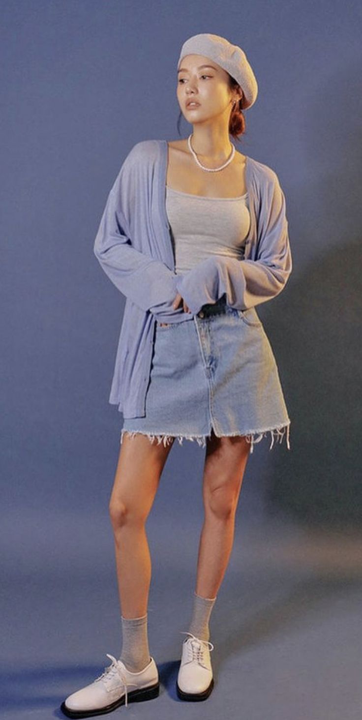 a full shot of a young woman posing in a studio. she is wearing a light blue cardigan, a light gray tank top, a light blue denim mini skirt, white socks, and white shoes. she's also wearing a light blue beret and a pearl necklace. the background is a solid light blue. the overall style is pastel and pretty.