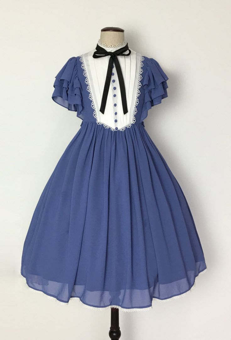a blue lolita fashion dress is shown on a mannequin. the dress is a light blue color with white accents. the top of the dress has a white blouse with a ruffled collar and sleeves. the skirt of the dress is full and flowing. the dress is accessorized with a black bow tie. the background is a plain white wall.