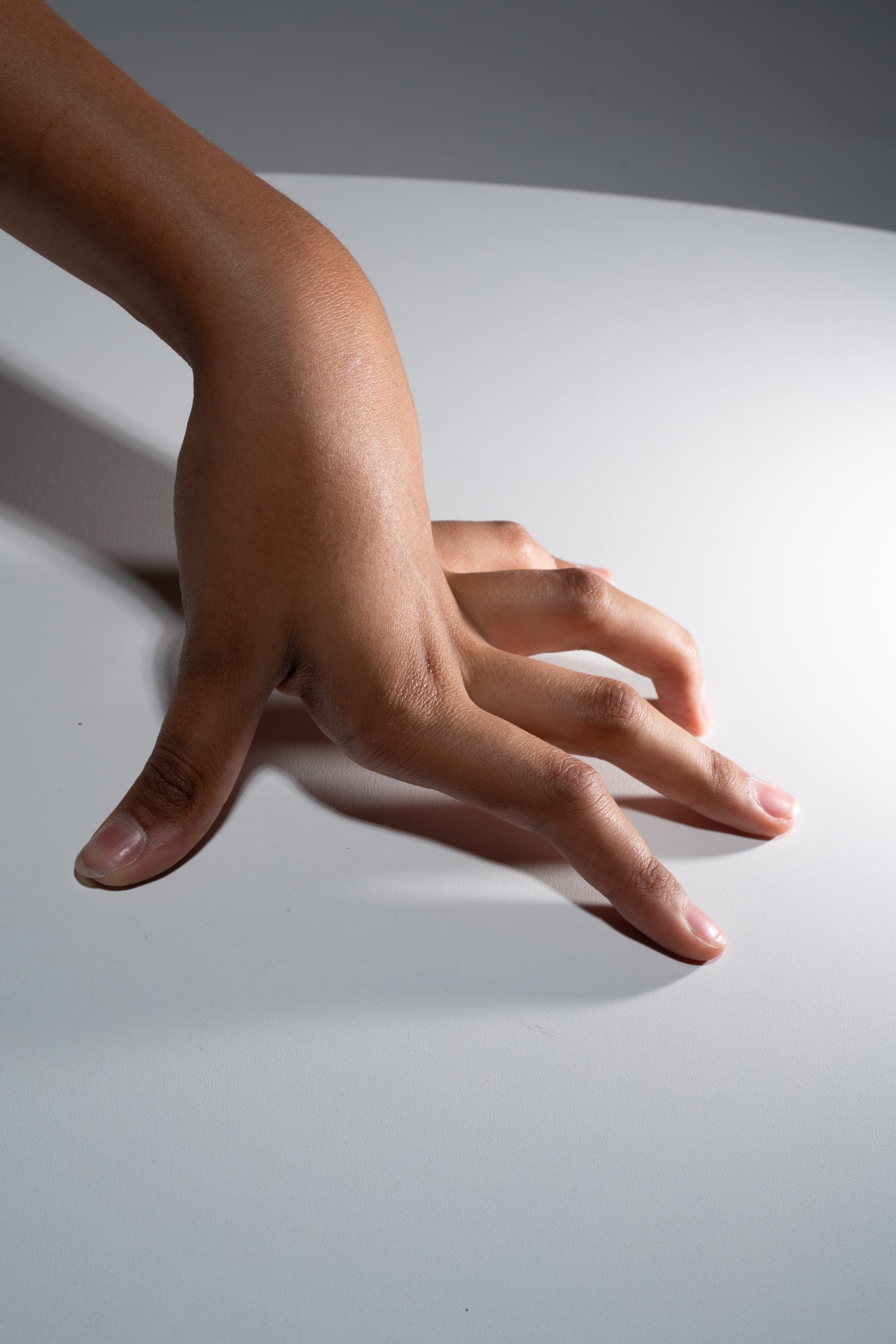 the image showcases a closeup of a hand with dark complexion delicately touching a smooth, white surface. the hand is outstretched, with fingers slightly spread, creating an impression of gentle exploration or tactile engagement with the surface. the studio lighting highlights the texture and contours of the skin, adding depth and dimensionality to the composition.