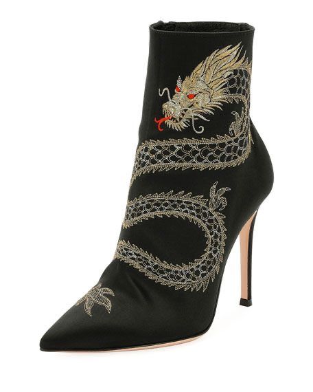 a closeup shot of a pair of elegant women's black satin ankle boots. the boots are adorned with intricate gold embroidery depicting a dragon wrapping around the shaft. the boots feature a pointed toe and stiletto heels, exuding a sophisticated and stylish look.  the background is plain white, focusing all attention on the boots.