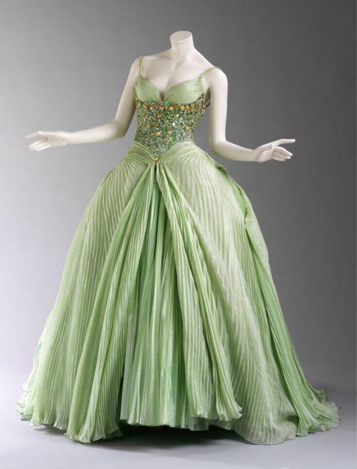 a long, elegant green dress is displayed on a mannequin. the dress features a beaded bodice and a pleated skirt that cascades to the floor.