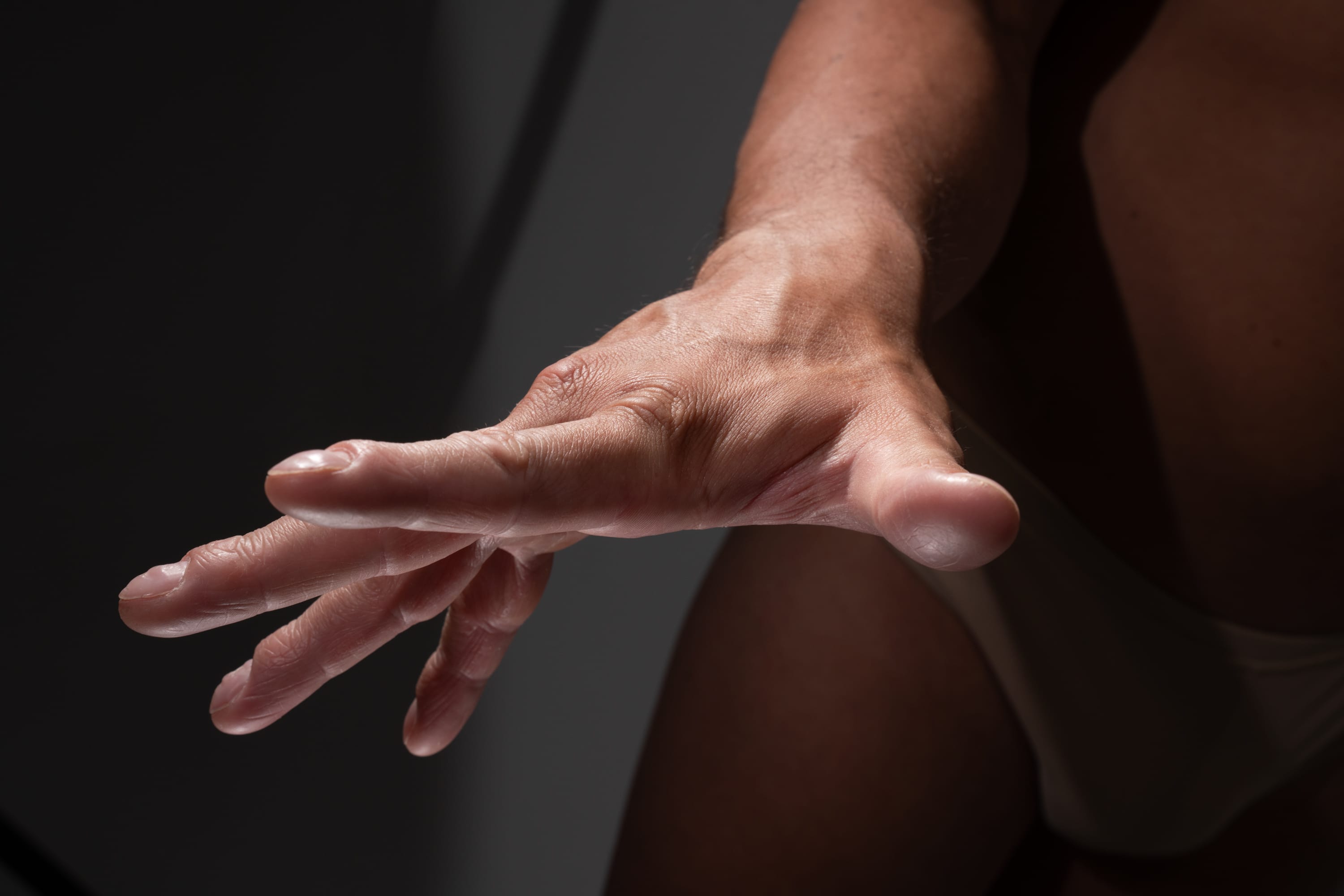 a close up shot of a man's hand and arm extended forward, illuminated by studio lighting which casts shadows on his body and the background. the focus is on the anatomy and gesture of the hand, highlighting its form and details.