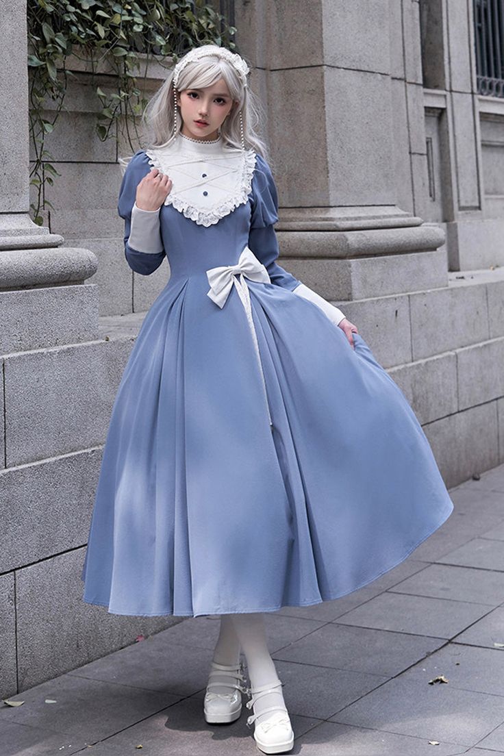 a young woman is posing in a blue and white lolita fashion dress. the dress has a full skirt and long sleeves, and is decorated with lace and a bow. she is also wearing white tights, white shoes, and a headband. the background is a stone building. the image is lit by natural light, and the perspective is at eye level.