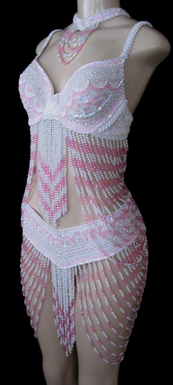 a mannequin is wearing a pink and white beaded belly dance costume with a necklace. the costume includes a bra, a skirt, and a beaded top. the mannequin is set against a black background.