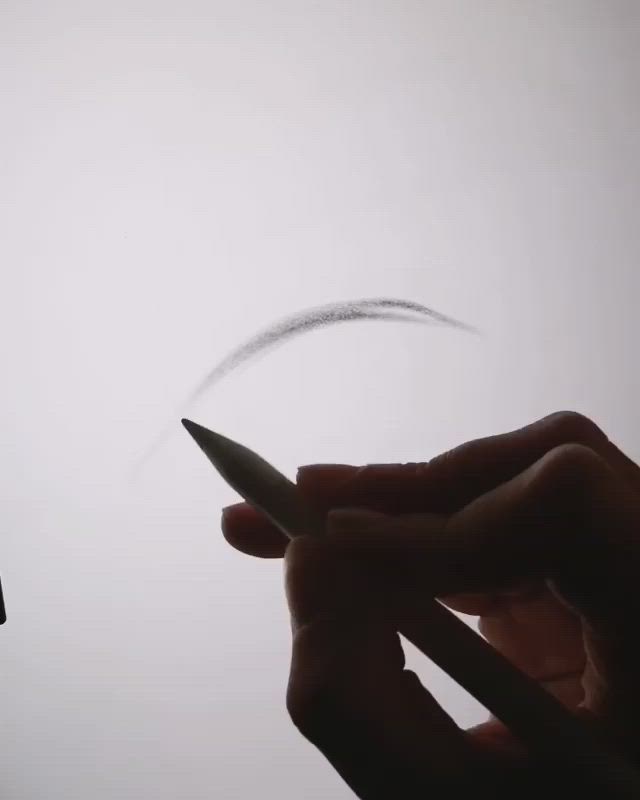 a hand is holding a white pencil drawing a grey line on a white surface.  the hand is in focus while the line is slightly blurry. the surface is bright white.