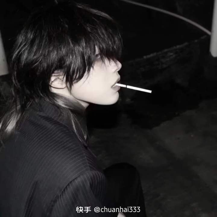 a black and white portrait of a young asian man with a stylish haircut, smoking a cigarette. he is wearing a dark, pinstriped shirt and his expression is contemplative. the background is dark and blurred, adding to the overall moody and edgy atmosphere of the image.