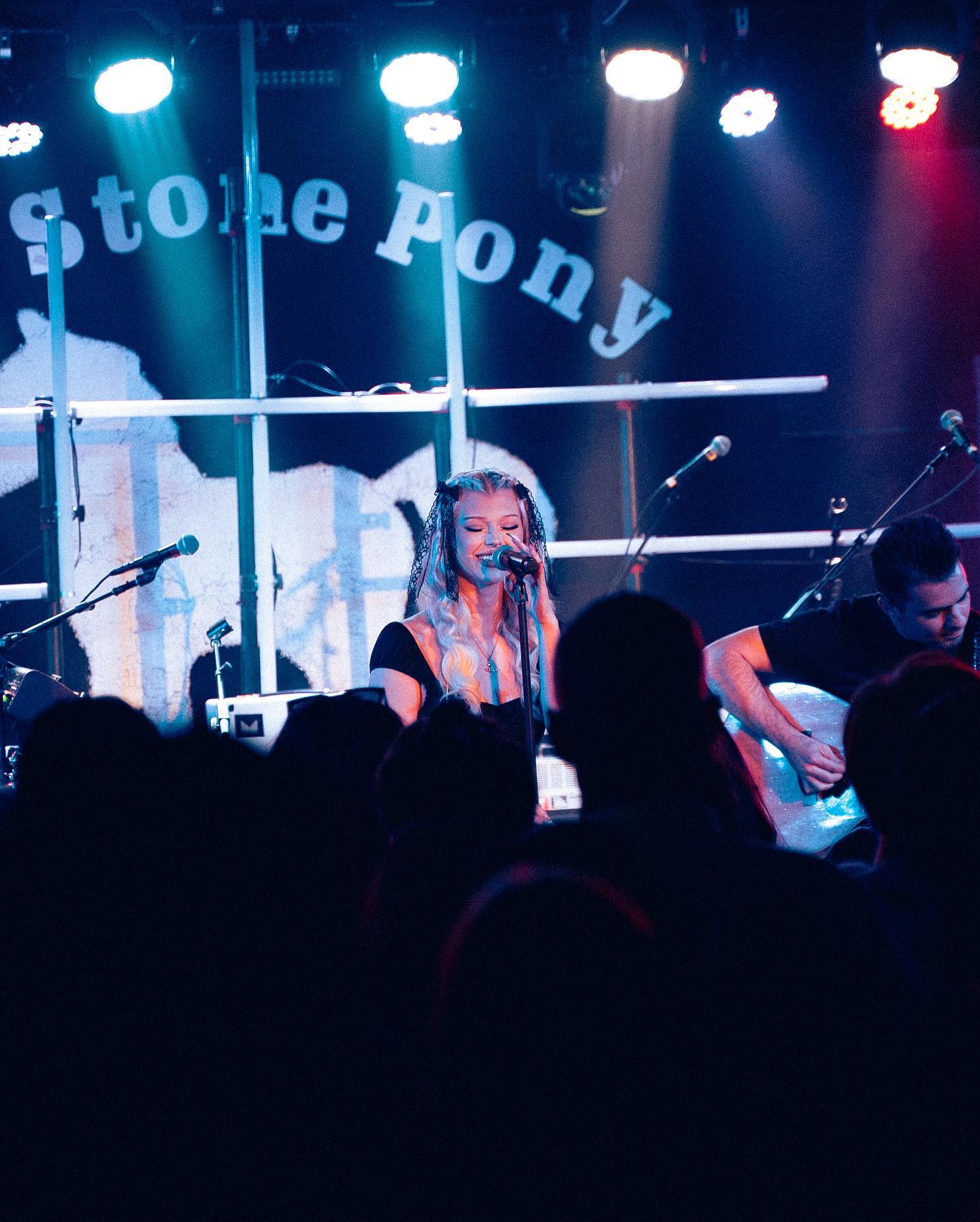 a live band performs at a venue called stone pony, with a blonde female singer at the microphone and a guitarist on the right, in front of a large crowd.
