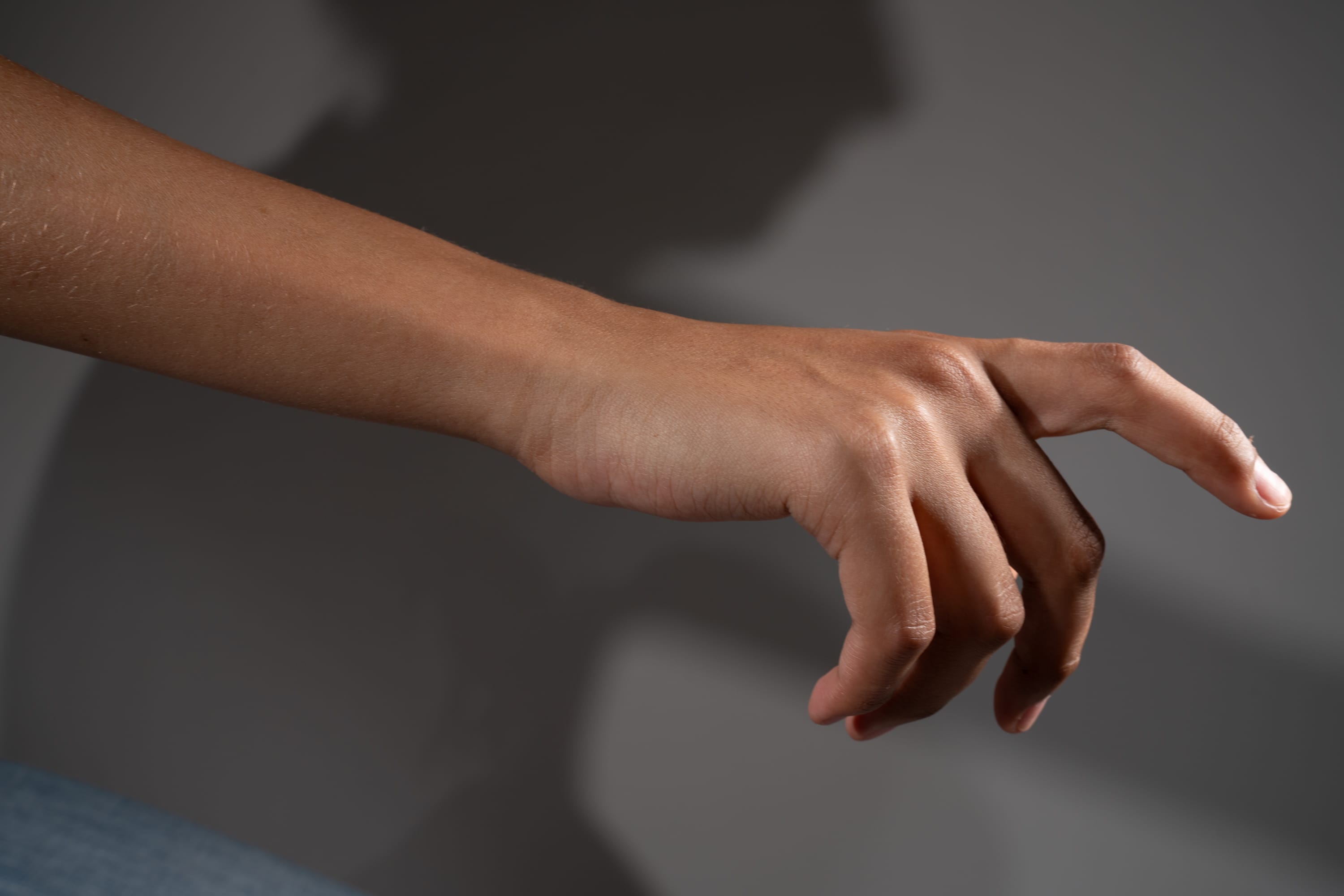a hand with its index finger extended. the hand has brown skin. the background is gray and features a shadow of the hand and presumably the person it is attached to.