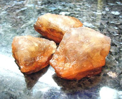 three translucent, brown rocks, possibly a type of quartz, are closeup on a rough gray background, with the surface reflecting the light.