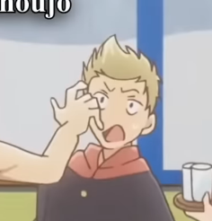 a closeup shot of an anime boy with short blonde hair and blue eyes wearing a black and red school uniform. he's being slapped on the forehead by another person, whose arm is visible on the left. the slap has caused his eyes to widen and his mouth to open in shock. the background features a light blue wall and a window frame. on the right side, there's a tray with two white cups, suggesting a possible school setting. the lighting is bright and the art style is typical of anime.
