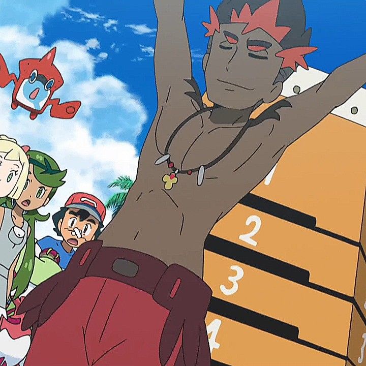 the image shows a male anime character with his arms raised and smiling. he is shirtless and has a necklace on. he is also wearing red shorts. behind him are other characters, one of whom is also shirtless and has a more toned physique. the image is likely from an anime show. the background shows a blue sky with white clouds.