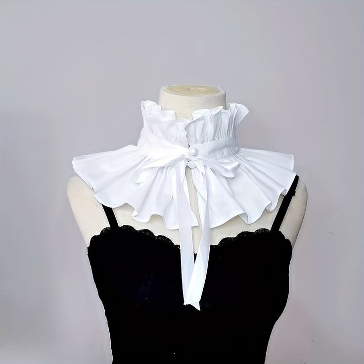 closeup view of a white cotton ruffle collar,  delicately crafted with multiple layers of ruffles and a bow tie in the center. it is displayed on a mannequin torso wearing a black top. the collar is reminiscent of victorian or gothic lolita styles, suggesting its use as a fashionable or costume accessory.  the overall aesthetic is elegant and refined.