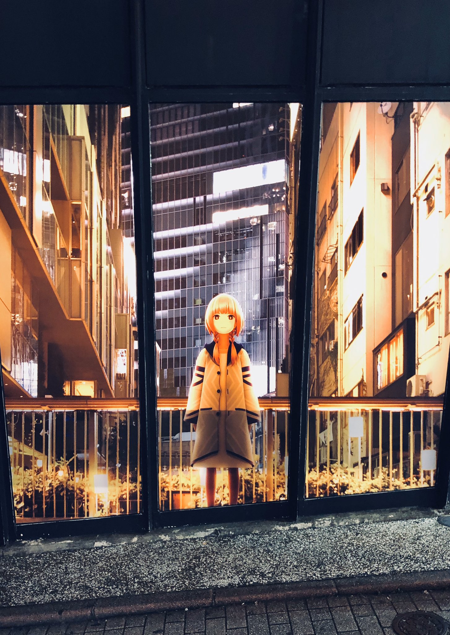 a poster featuring an anime girl in a yellow coat stands illuminated against a nighttime cityscape. the backdrop showcases a realistic depiction of urban buildings and a bridge, creating a blend of animation and realworld scenery. the girl, positioned centrally, draws the viewer's eye with her bright attire contrasting against the darker urban setting.  the scene is captured at street level, providing an immersive perspective.