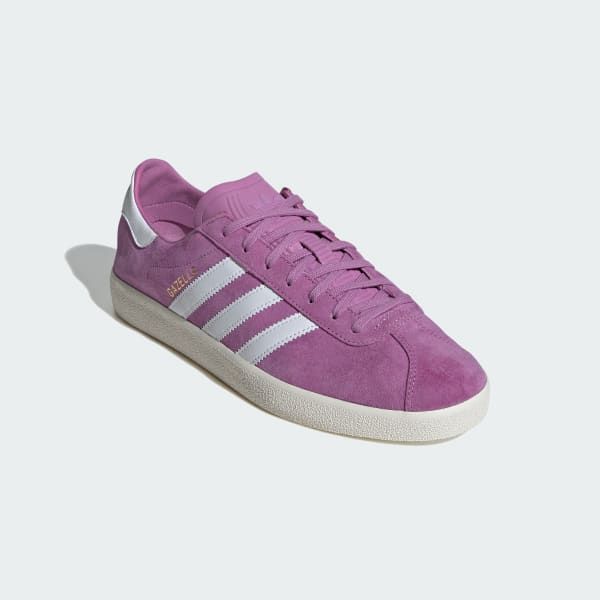 a pair of pink adidas gazelle sneakers with white stripes. the sneakers are made of suede and have a white sole. the image shows the shoes from the side.
