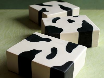 three ceramic blocks with black and white cow print design stacked on top of each other on a green surface. the blocks are square and made from white ceramic with black spots painted on.
