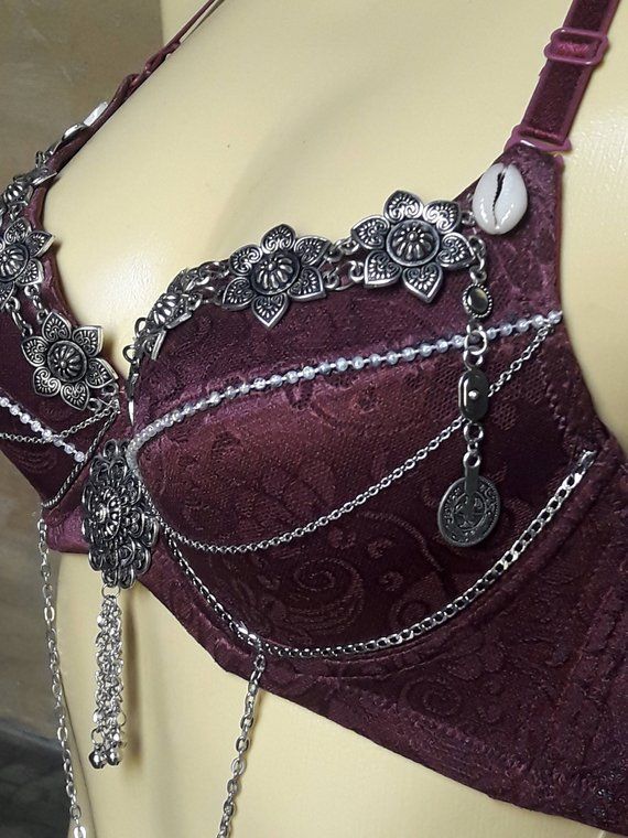 a closeup of a burgundy bra with intricate floral silver embellishments and chains. the bra is decorated with a delicate silver design and chains, creating a bohemian and elegant look.