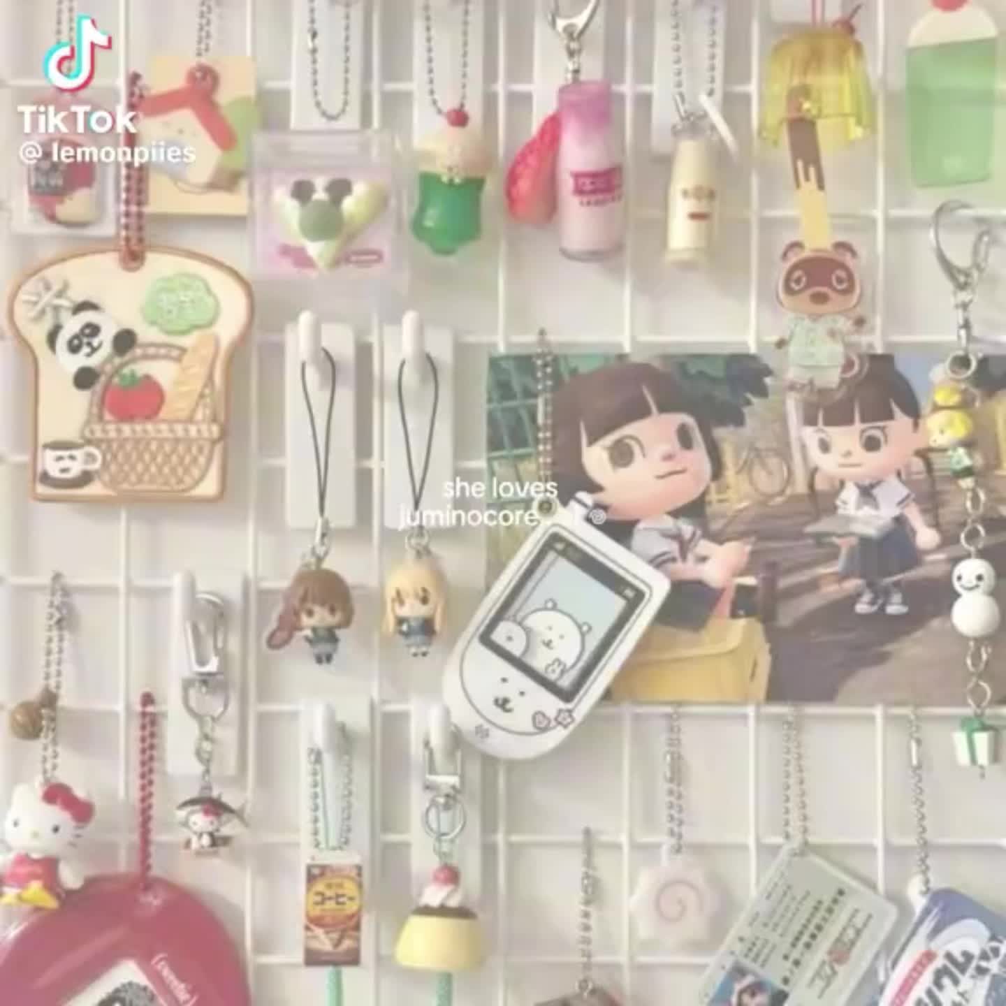 a closeup shot of a wall grid adorned with various keychains. there are several keychains featuring characters from the video game animal crossing, along with other cute items like a panda on a piece of bread, japanese snacks, a strawberry milk carton, and pudding. the overall aesthetic is kawaii and appears to be part of a collection or display. a tiktok watermark is visible in the upper left corner.