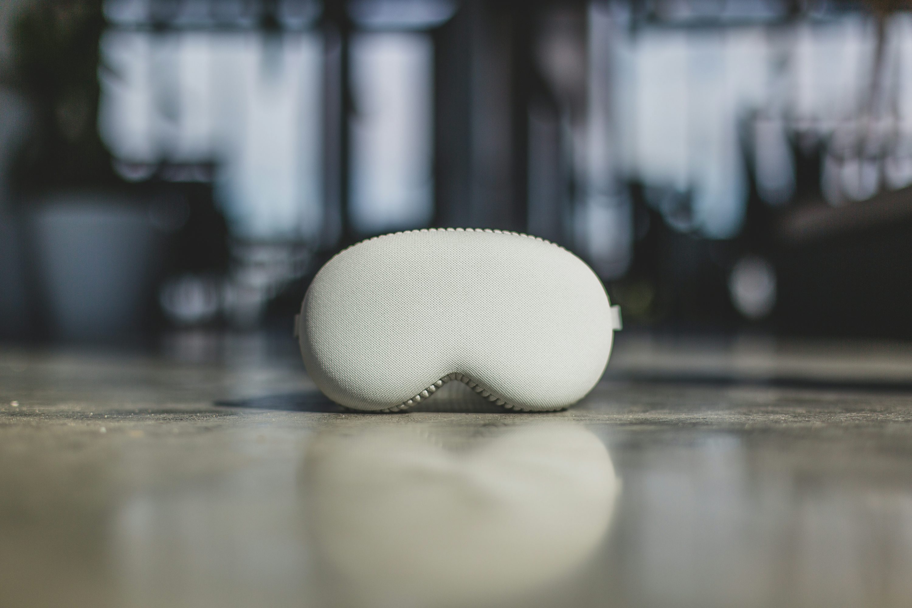 a closeup shot showcases a white sleep mask resting on a reflective surface, likely a floor. the sleep mask is characterized by its soft and textured appearance, suggesting a focus on comfort and relaxation. its shape is reminiscent of an oval with a curved section for the nose bridge, and the mask is designed to block out light for improved sleep quality. the glossy floor reflects the sleep mask, creating a mirror image and emphasizing its presence in the scene. the background is blurred, indicating a shallow depth of field, which helps to draw attention to the sleep mask as the primary subject. overall, the image conveys a sense of tranquility and suggests the importance of sleep and selfcare.