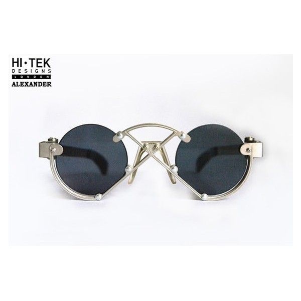 a pair of round sunglasses with silver frames and black lenses are centered on a white background. the brand logo "hitek designs london alexander" is in the upper left corner. the sunglasses have a distinctive design with exposed metal framing around the lenses and across the bridge of the nose, punctuated by small silver balls.