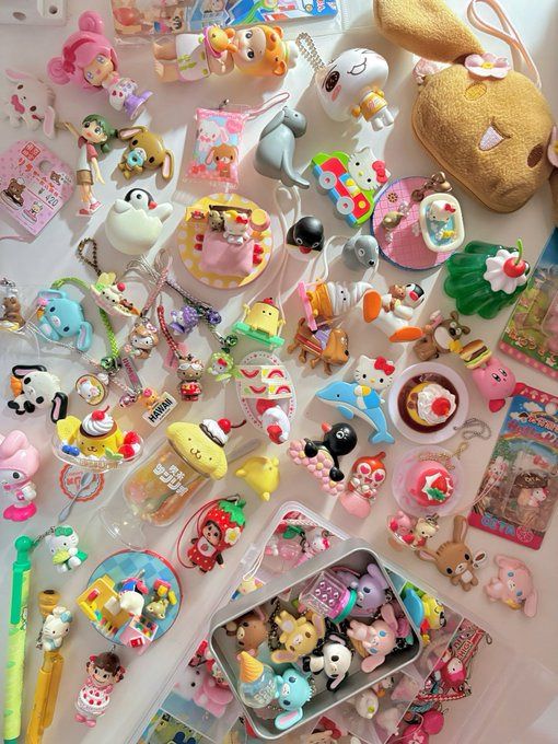 the image showcases a collection of various toys and keychains, predominantly featuring sanrio characters like hello kitty and other kawaiistyle figurines. there are also charms, bunnies, dessertthemed items, and other animal characters within the collection. they are arranged in a haphazard manner, some within a small metal tin. the image conveys a sense of childhood nostalgia and a love for collecting.