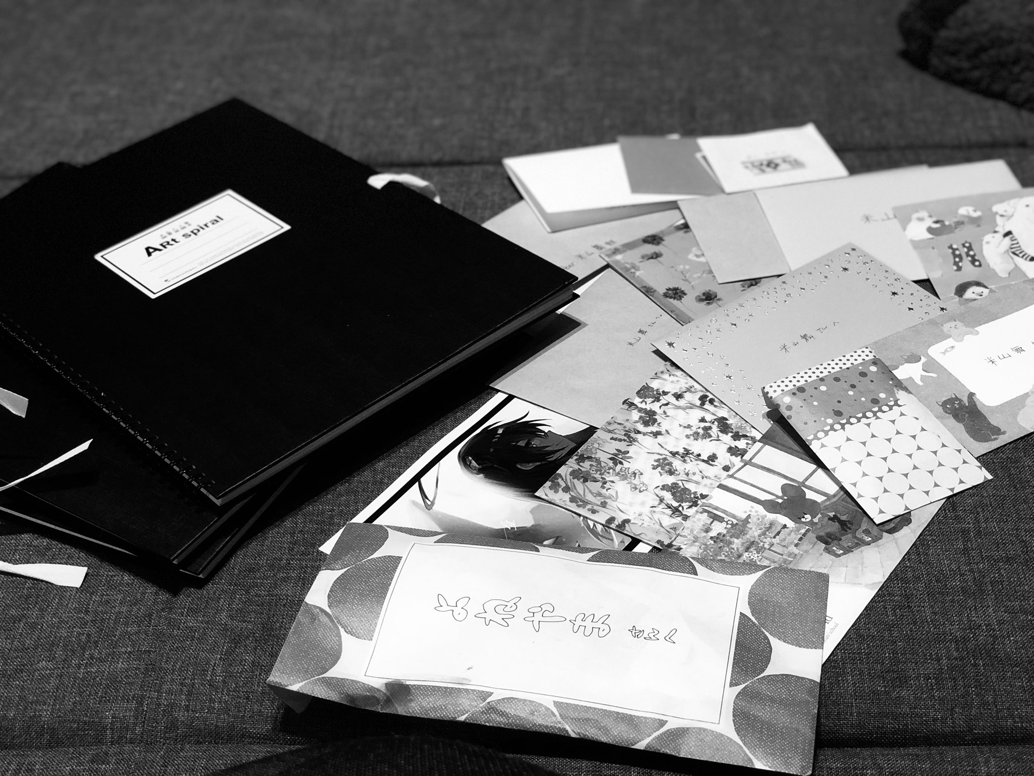 the image shows a collection of fan mail and gifts, including a black portfolio labeled "art spiral," various envelopes with illustrations, and a larger envelope with a handwritten message. the items are arranged on a gray surface, possibly a sofa or bed. the black and white photography emphasizes the personal and heartfelt nature of the gifts.