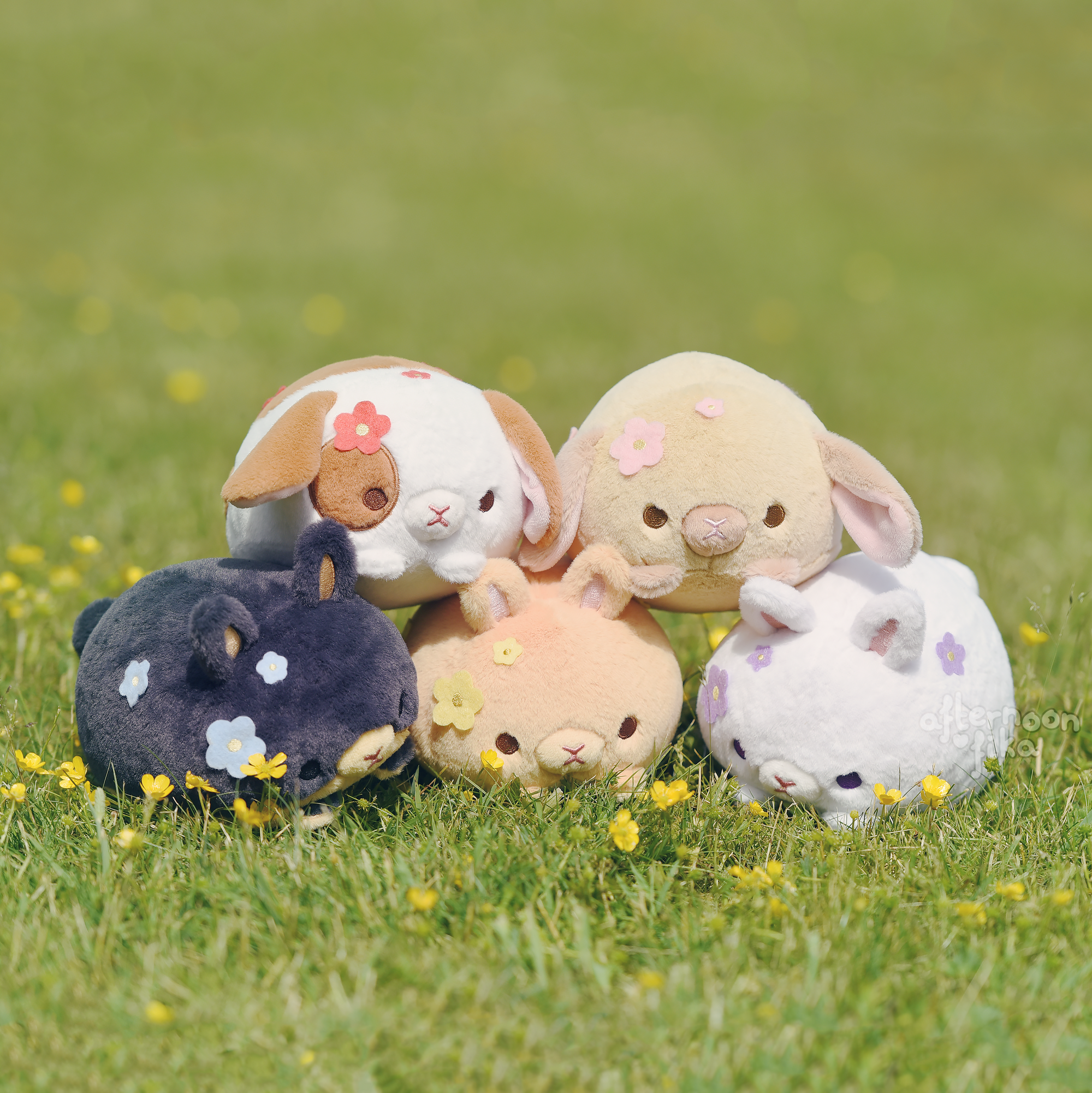 ive adorable plush toys, resembling bunnies and rabbits, are nestled together in a grassy field. each toy is pastelcolored and adorned with small, fabric flowers.  they are arranged in a closeknit group, suggesting a friendly collection. the setting is outdoors, with lush green grass visible in the background and around the toys, implying a spring or summertime scene. the overall aesthetic is undeniably kawaii, emphasizing cuteness and softness.