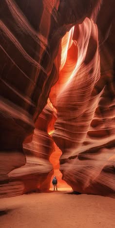 a single hiker stands in the middle of a narrow sandstone canyon.  the walls of the canyon are carved with intricate patterns and the light from the opening at the top of the canyon creates a beautiful glow.  this canyon is most likely located in antelope canyon, arizona.