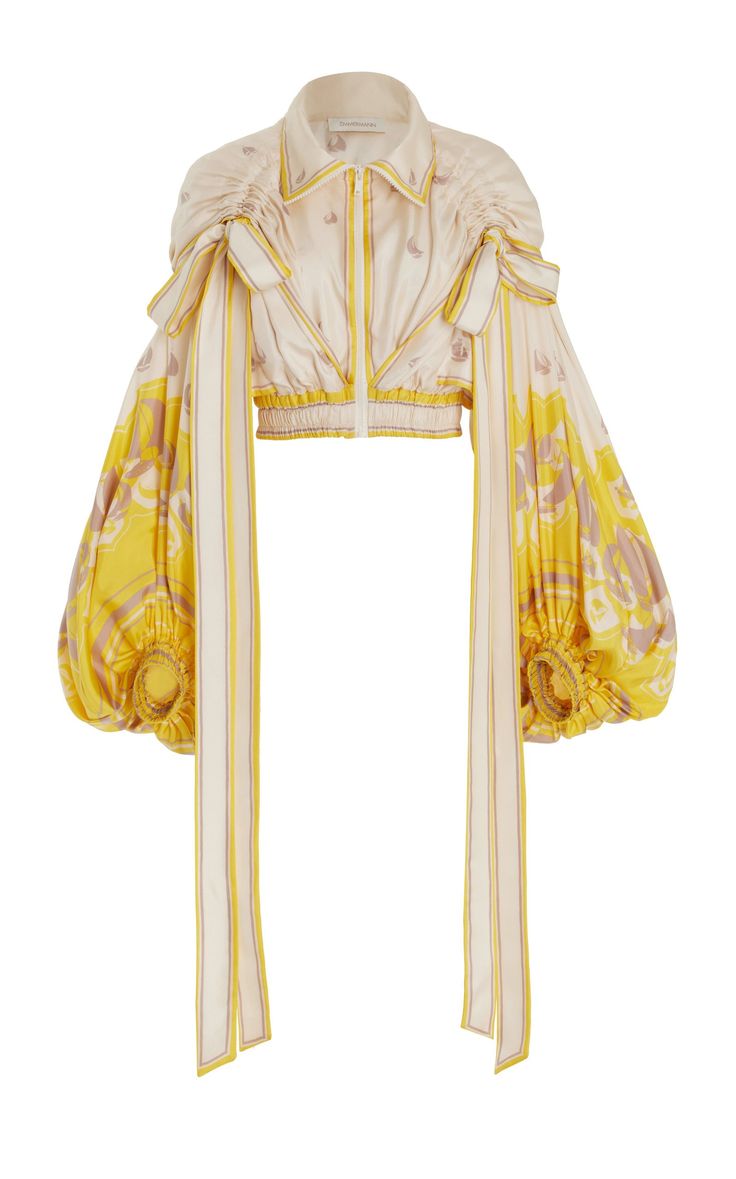 this is a closeup of a yellow floral print jacket with puff sleeves. the jacket is cropped and has a collar, zipper, bow tie, and belt. the background is white.