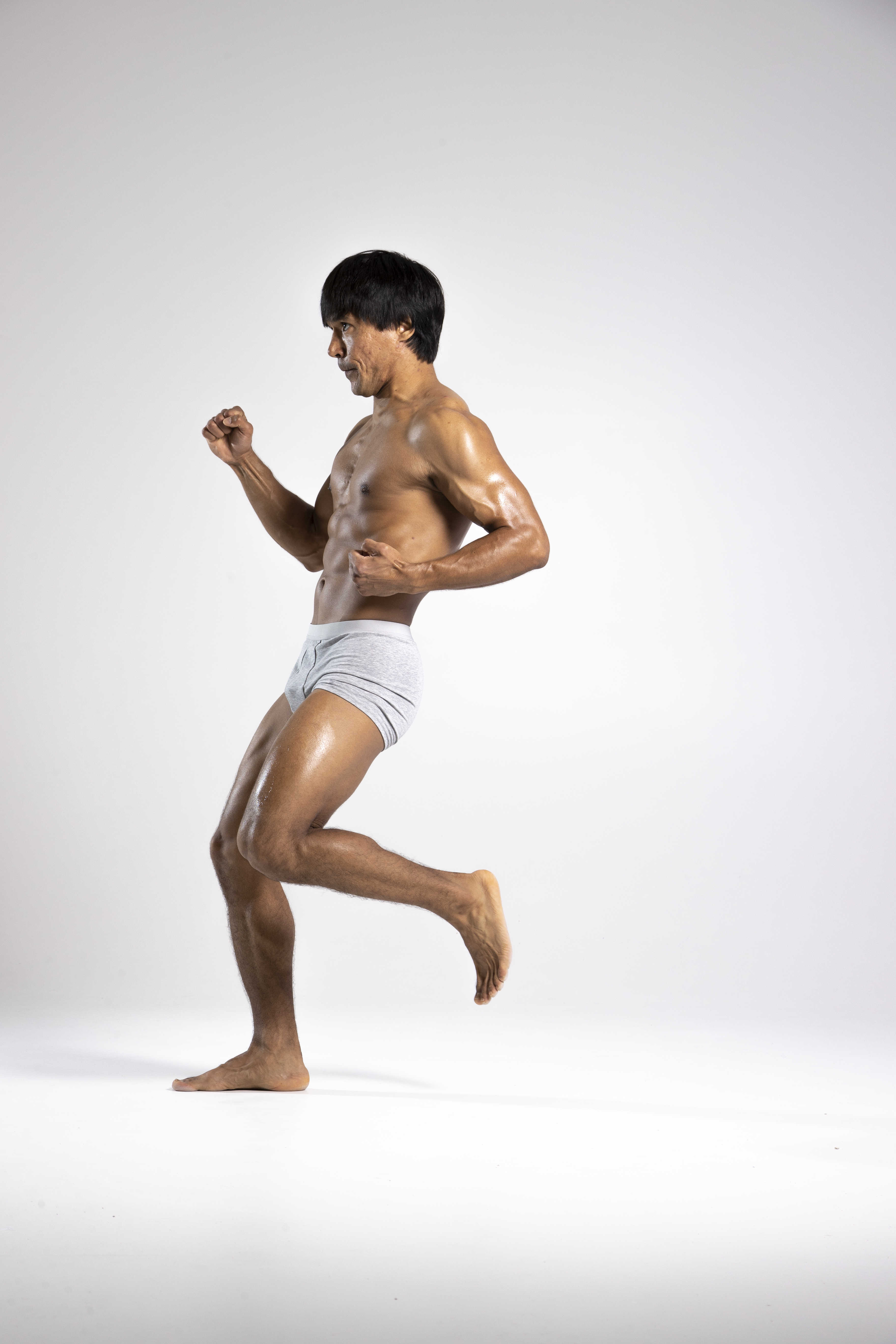 a shirtless man in grey underwear is in a fighting stance, on a white background. he is muscular and appears to be an athlete or someone involved in fitness. he is in a dynamic pose, seemingly ready to strike or move.