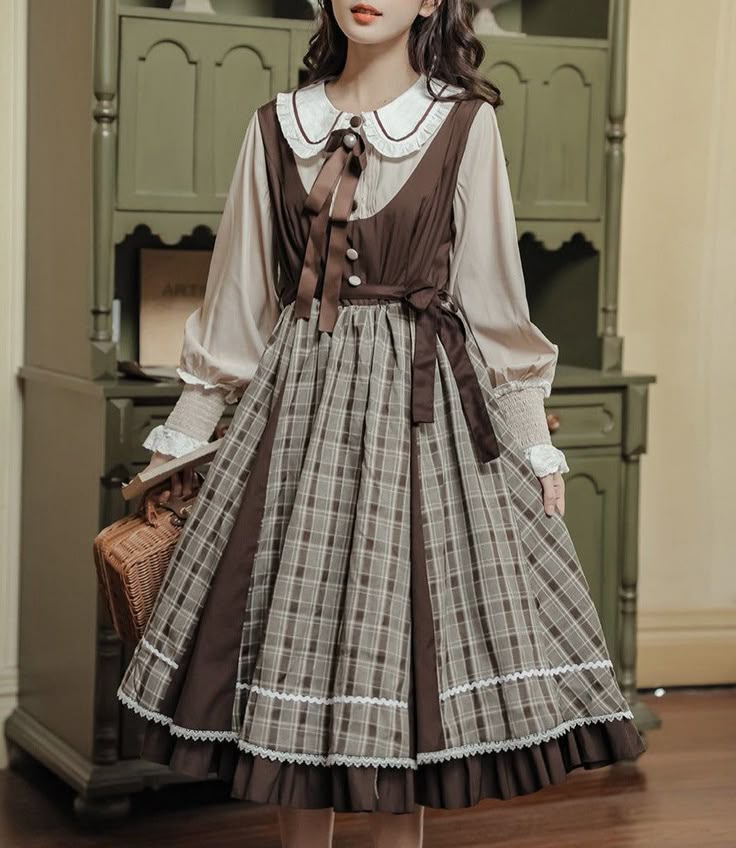a woman stands in front of an antique cabinet wearing a brown plaid lolita dress with a peter pan collar blouse and ribbons. she is holding a basket.