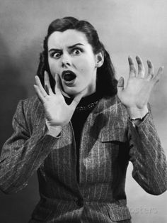 a black and white portrait of a woman with a shocked expression. she is wearing a pinstripe jacket and has her hands raised in a gesture of fear or surprise. her mouth is open in a gasp.