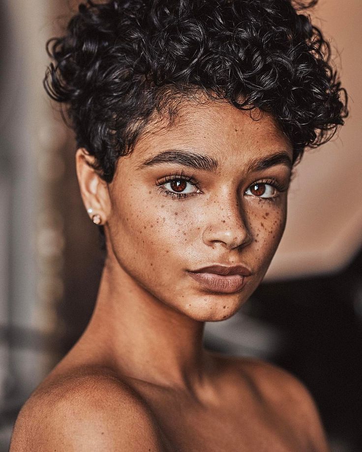 a closeup portrait of a woman with curly hair and freckles. she is facing the camera, and her face is the main focus. her skin is smooth, and her eyes are brown. she has a small earring in her left ear. her shoulders are bare.
