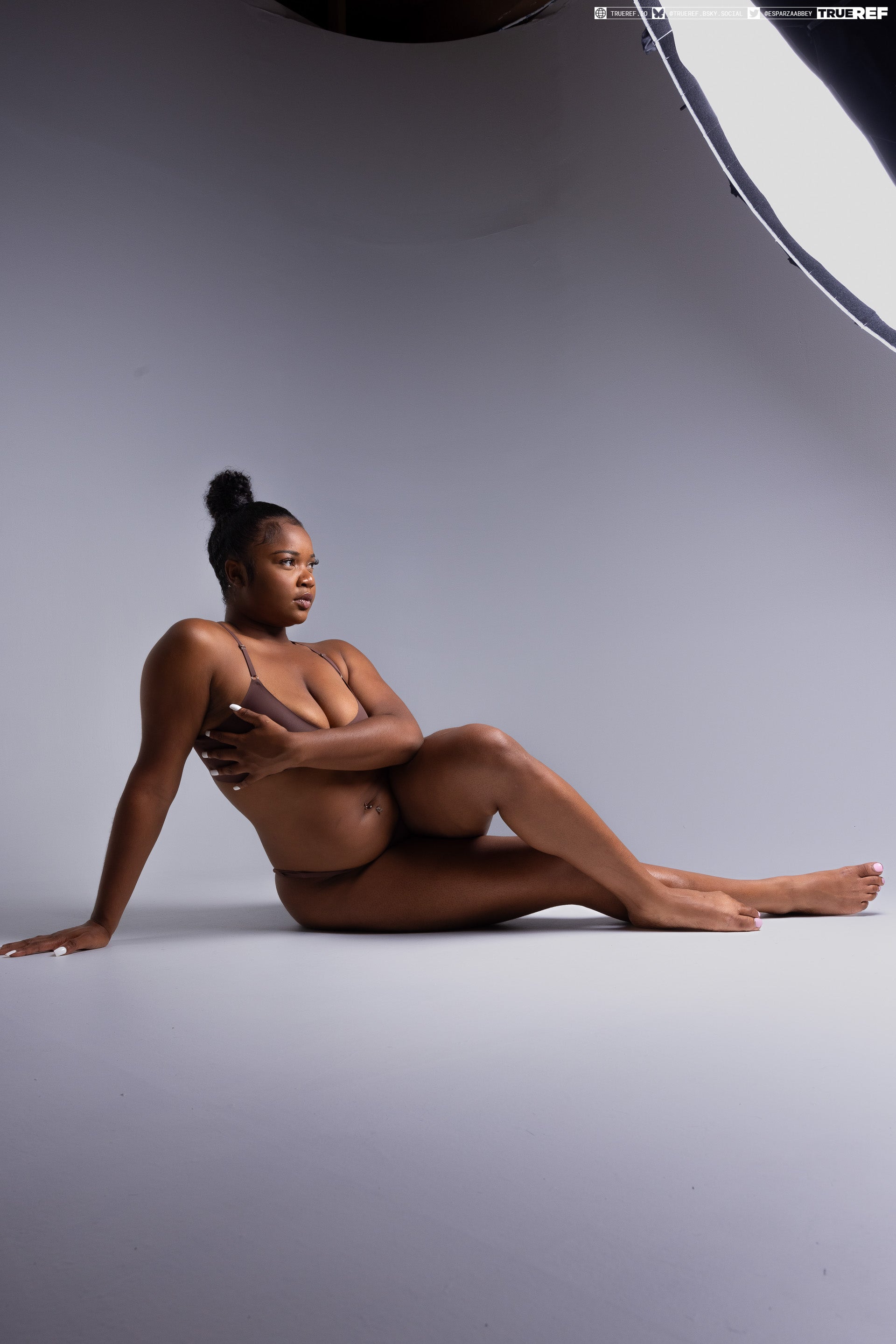 a woman is lying down in a studio, wearing lingerie. she is posing for the camera and has dark skin. she is brunette. she is wearing underwear.