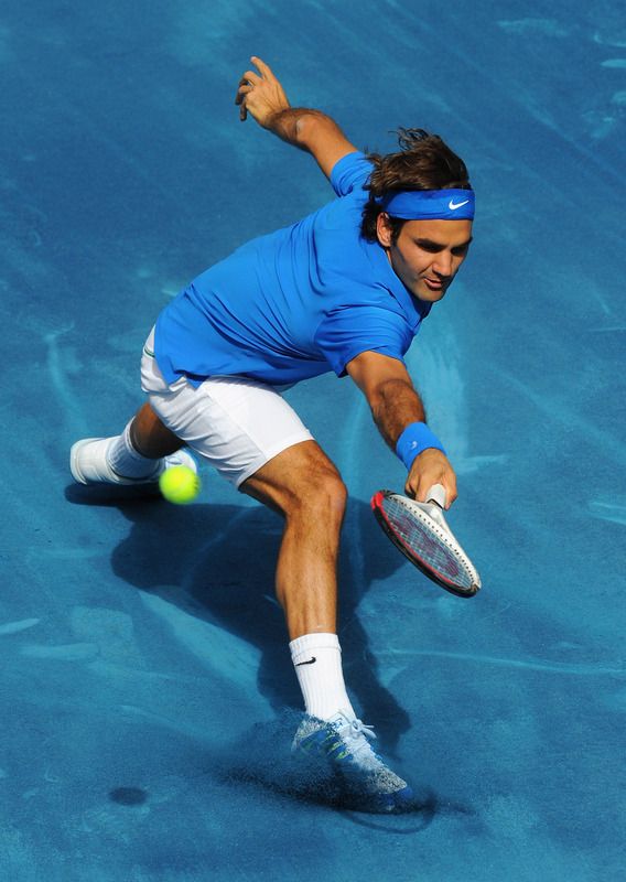 a male tennis player wearing a blue shirt and white shorts, is playing a tennis match. he is midswing, and the ball is in the air. the court is blue.